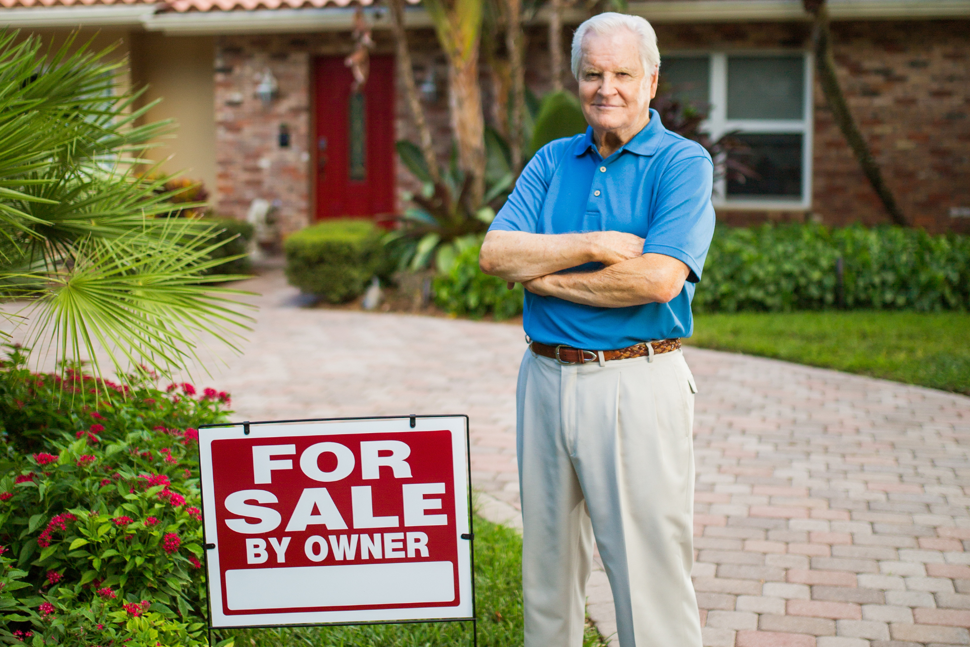 Man standing by a “For Sale by Owner” sign in front of a house and driveway