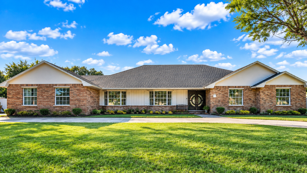 Single-story brick house with a wide front lawn under a bright blue sky