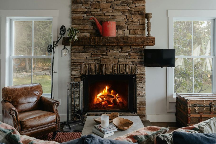 Cozy living room with stone fireplace, burning fire, leather chair, TV, and bright windows