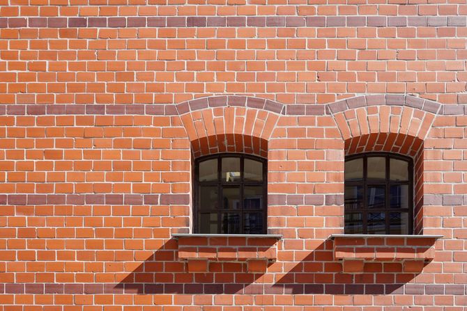Brick wall with two arched windows and striped shadows in sunlight
