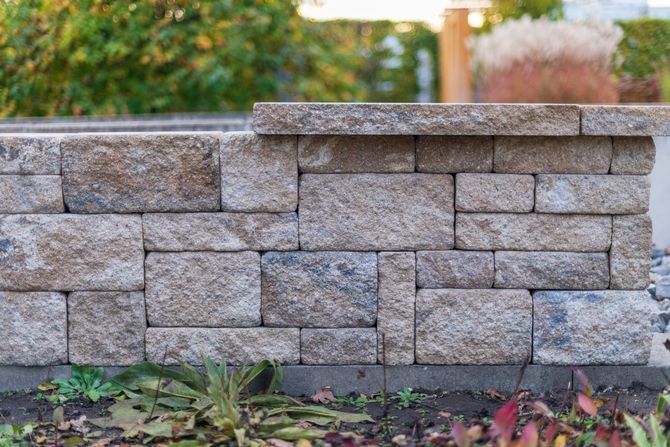 Stacked gray stone retaining wall in a garden with autumn leaves and blurred greenery behind it