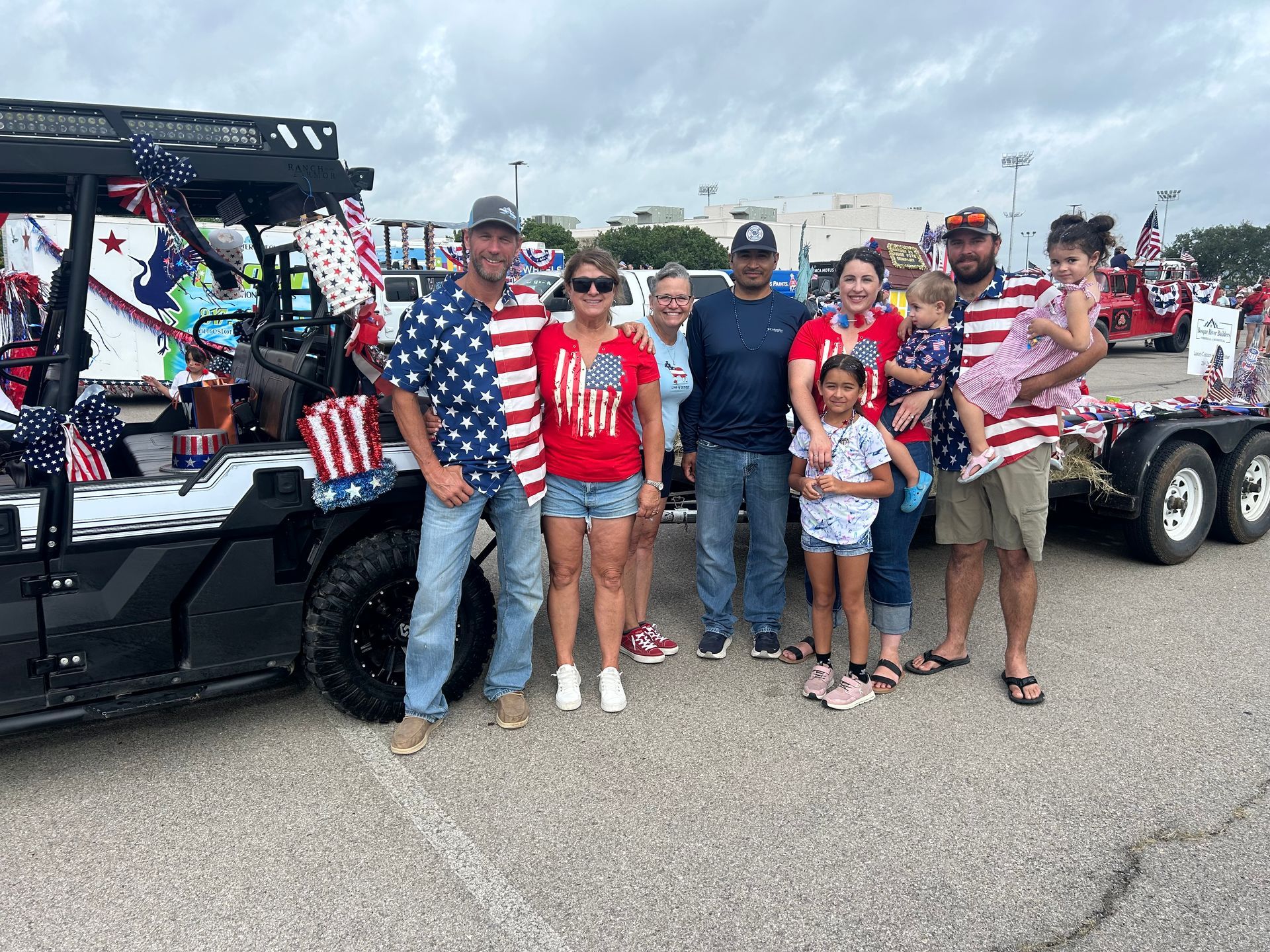 People posing with a patriotic vehicle decorated with flags and stars. Cloudy sky.