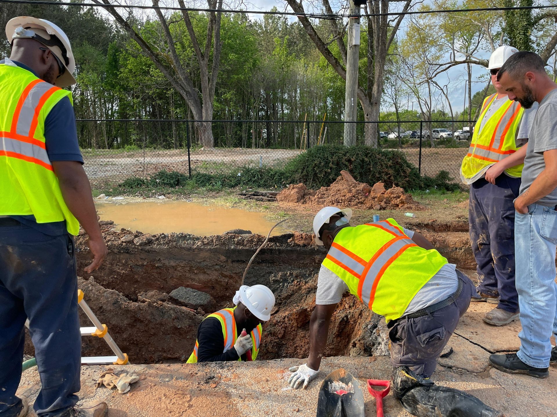 Construction workers in safety vests examining a flooded excavation site with exposed pipes.