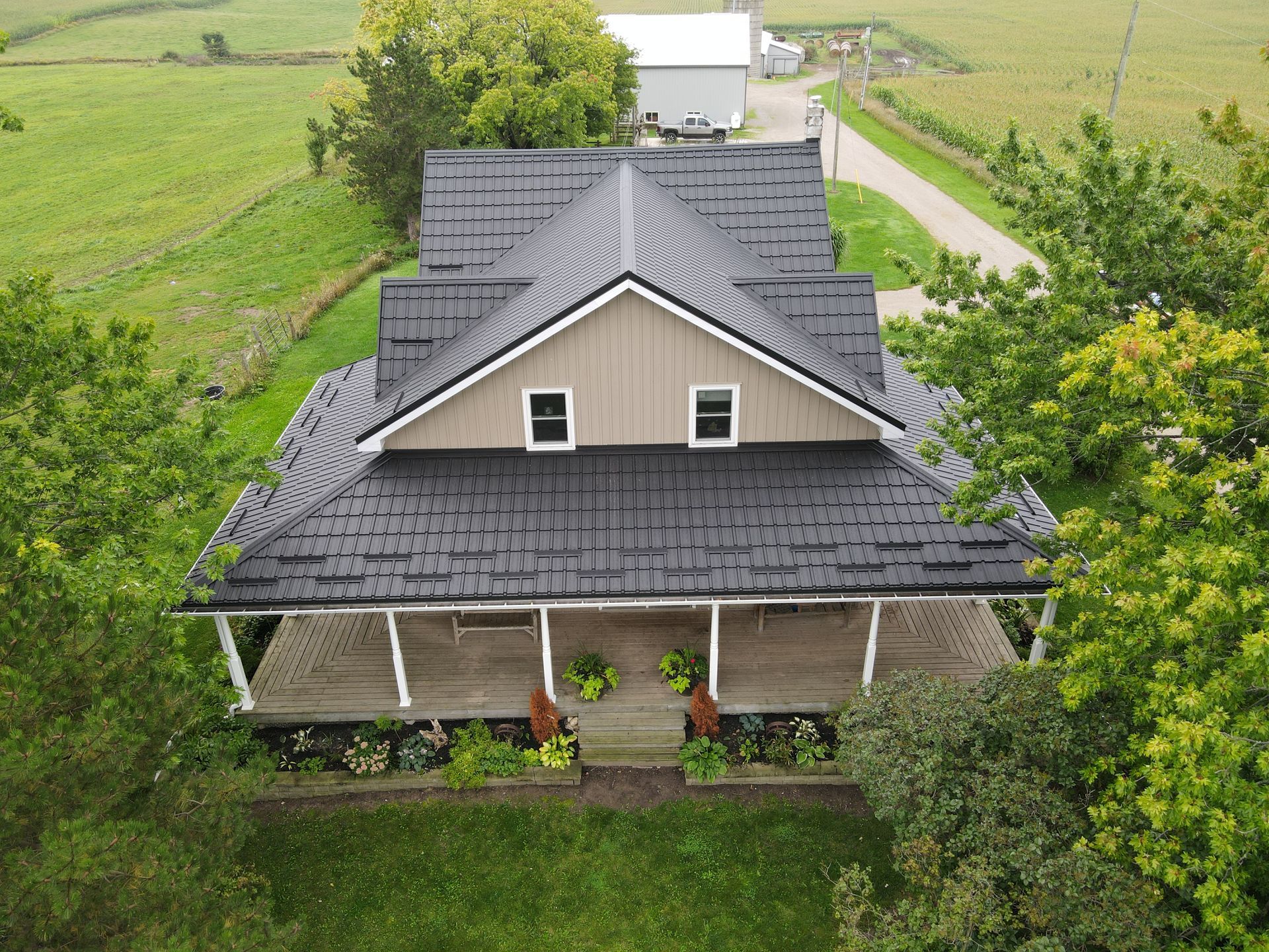 Aerial view of a gray-roofed farmhouse with a front porch, surrounded by green fields.