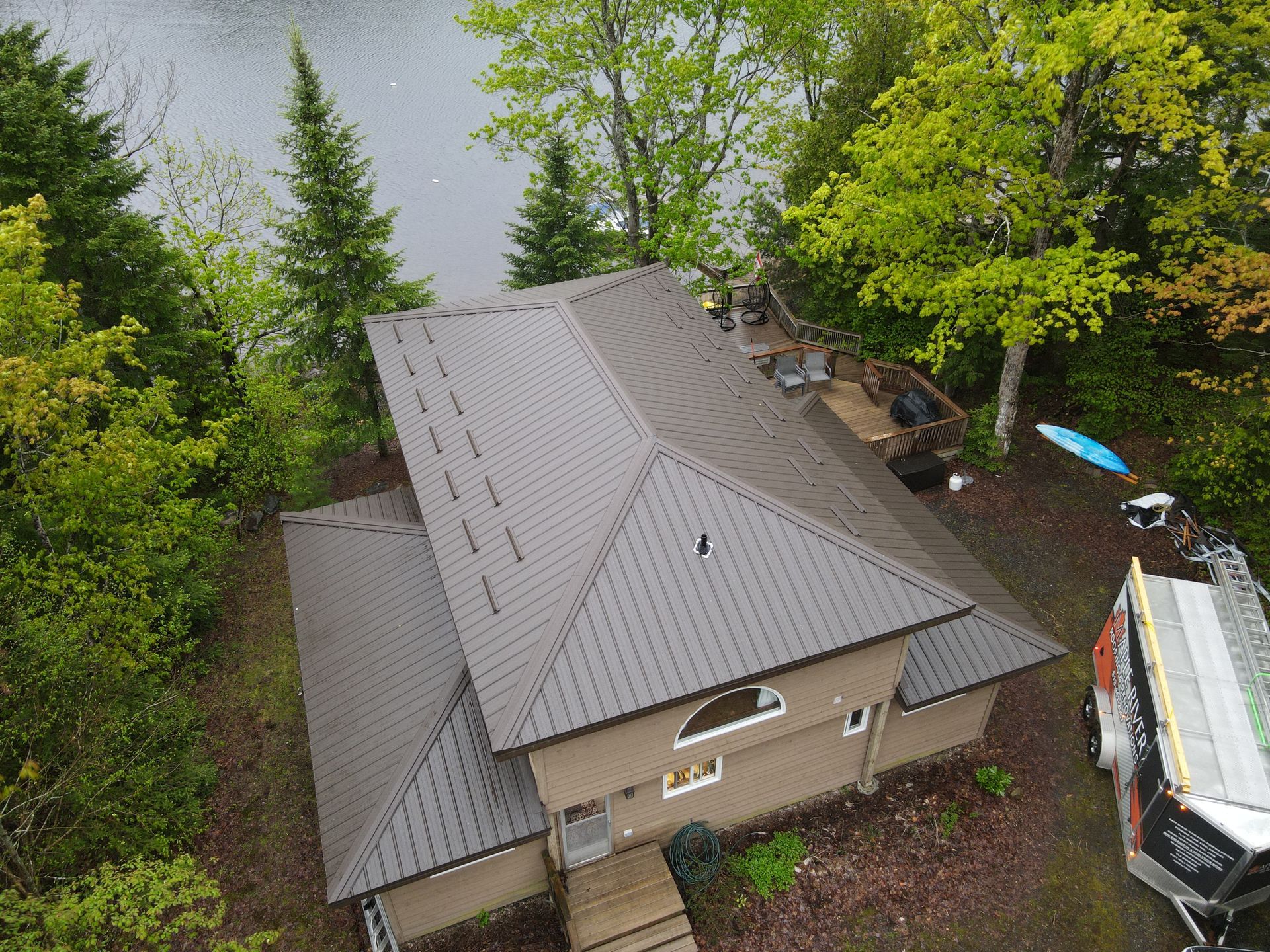 An aerial view of a house with a metal roof next to a lake.