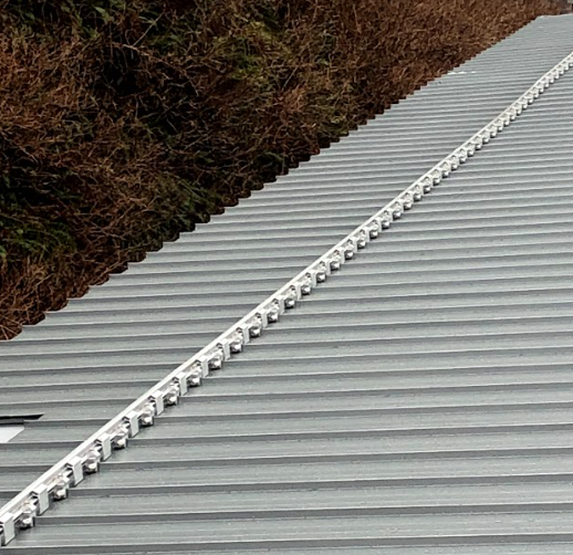 Gray corrugated metal roof with a long, white snow guard installed along the ridge.