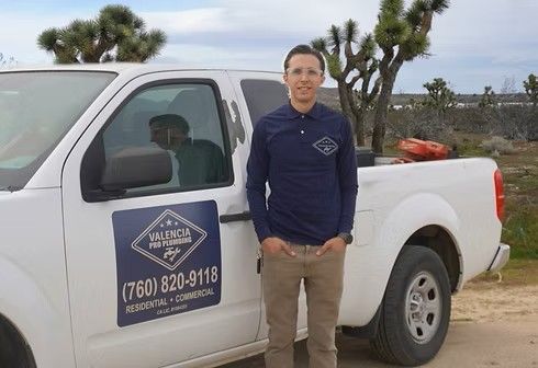 Man standing beside a white pickup truck with a company logo on the door in a desert roadside setting