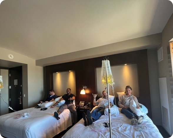 A group of people are sitting on a bed with an iv in a hotel room
