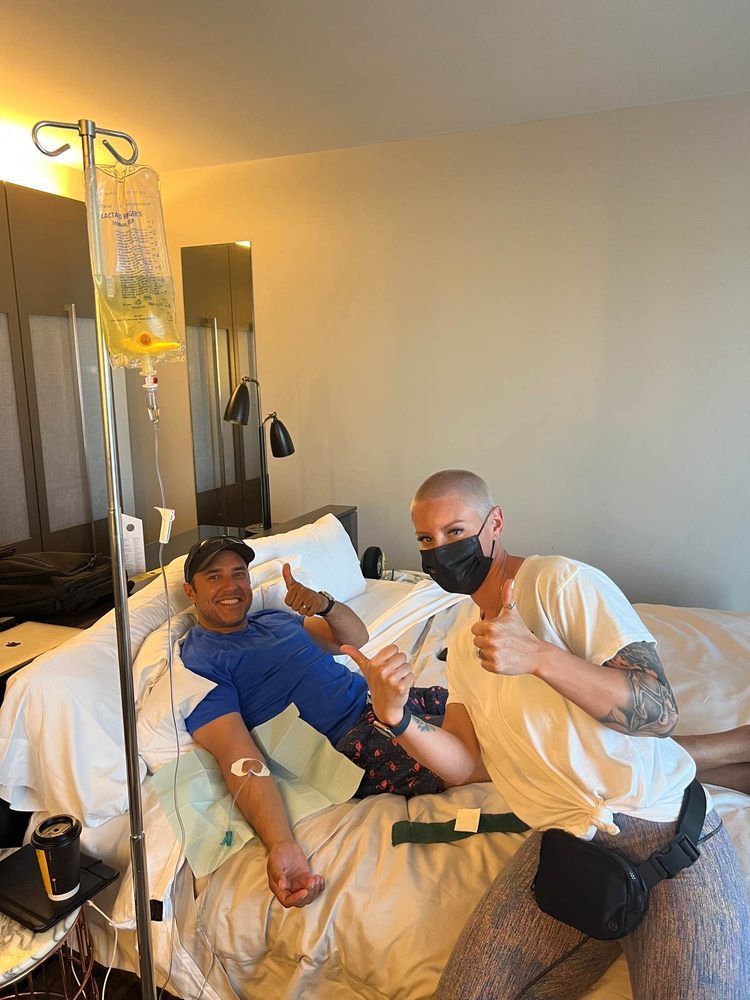 Two men are sitting in a hospital bed giving thumbs up.