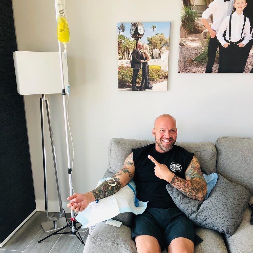 A man with tattoos is sitting on a couch giving a thumbs up