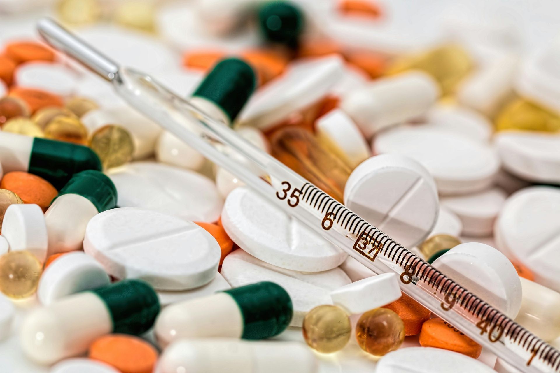 Pile of pills and capsules with a thermometer, various colors.