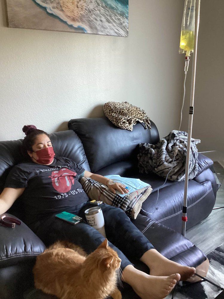 A woman wearing a mask is sitting on a couch with a cat.