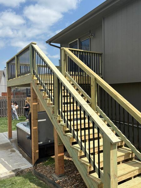 Outdoor wooden staircase with yellow railings leading to a raised deck beside a house.