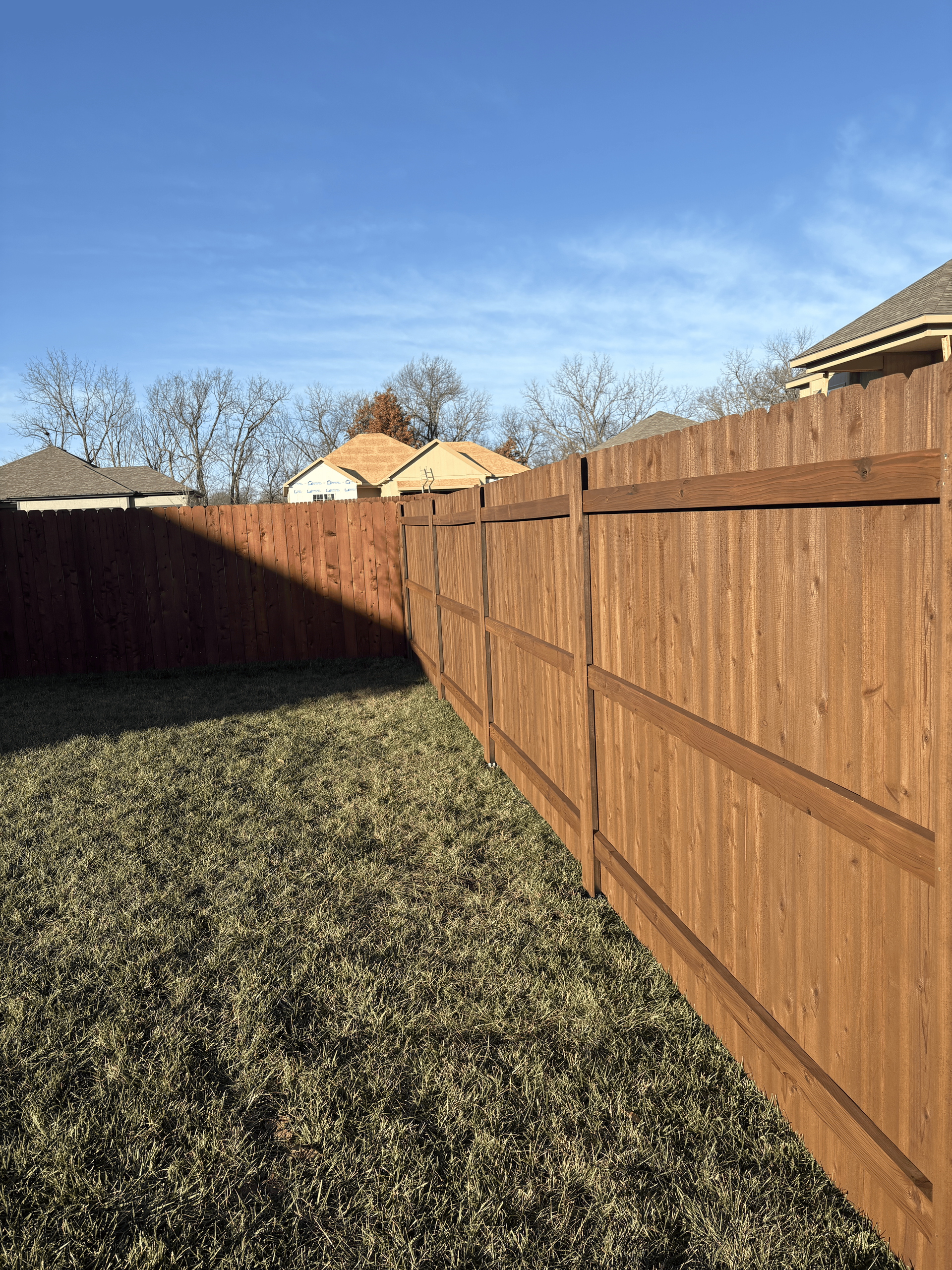 Backyard with a wooden fence, patchy grass, and a clear blue sky on a sunny day
