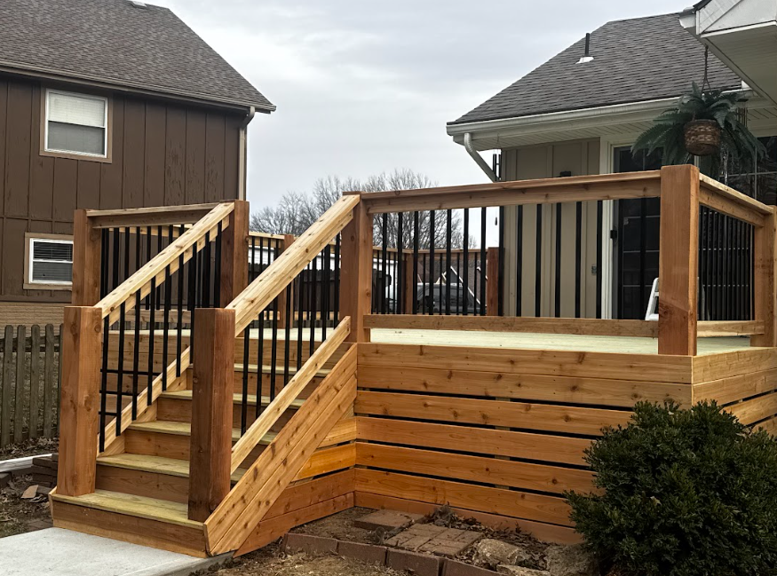 Wooden backyard deck with stairs and railing between two houses under an overcast sky