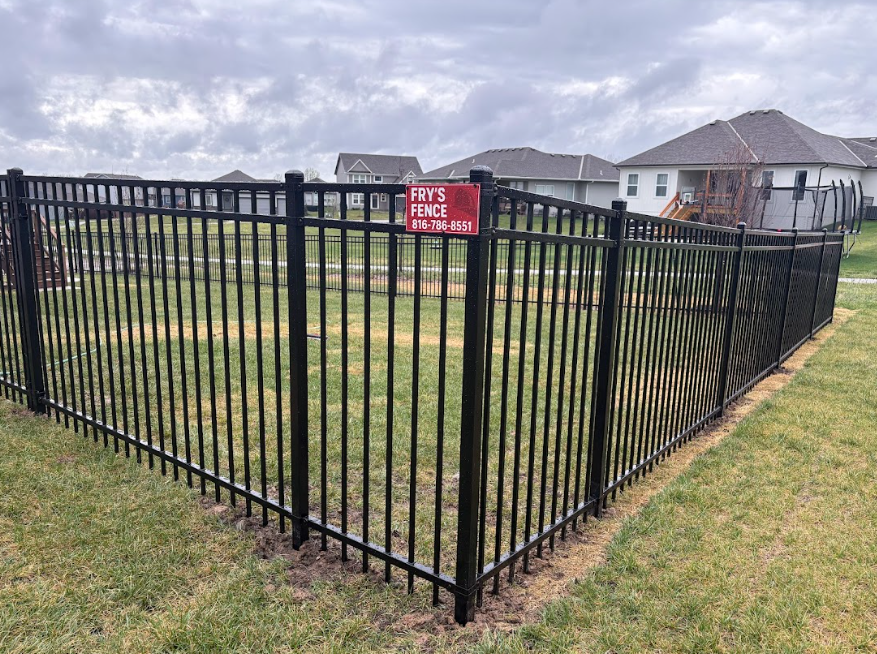 Black metal fence around grassy yard with a red “HOG PEN” sign in a suburban neighborhood