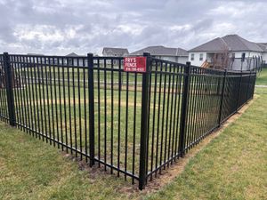 Black metal fence around a grassy yard with a red warning sign in a suburban neighborhood