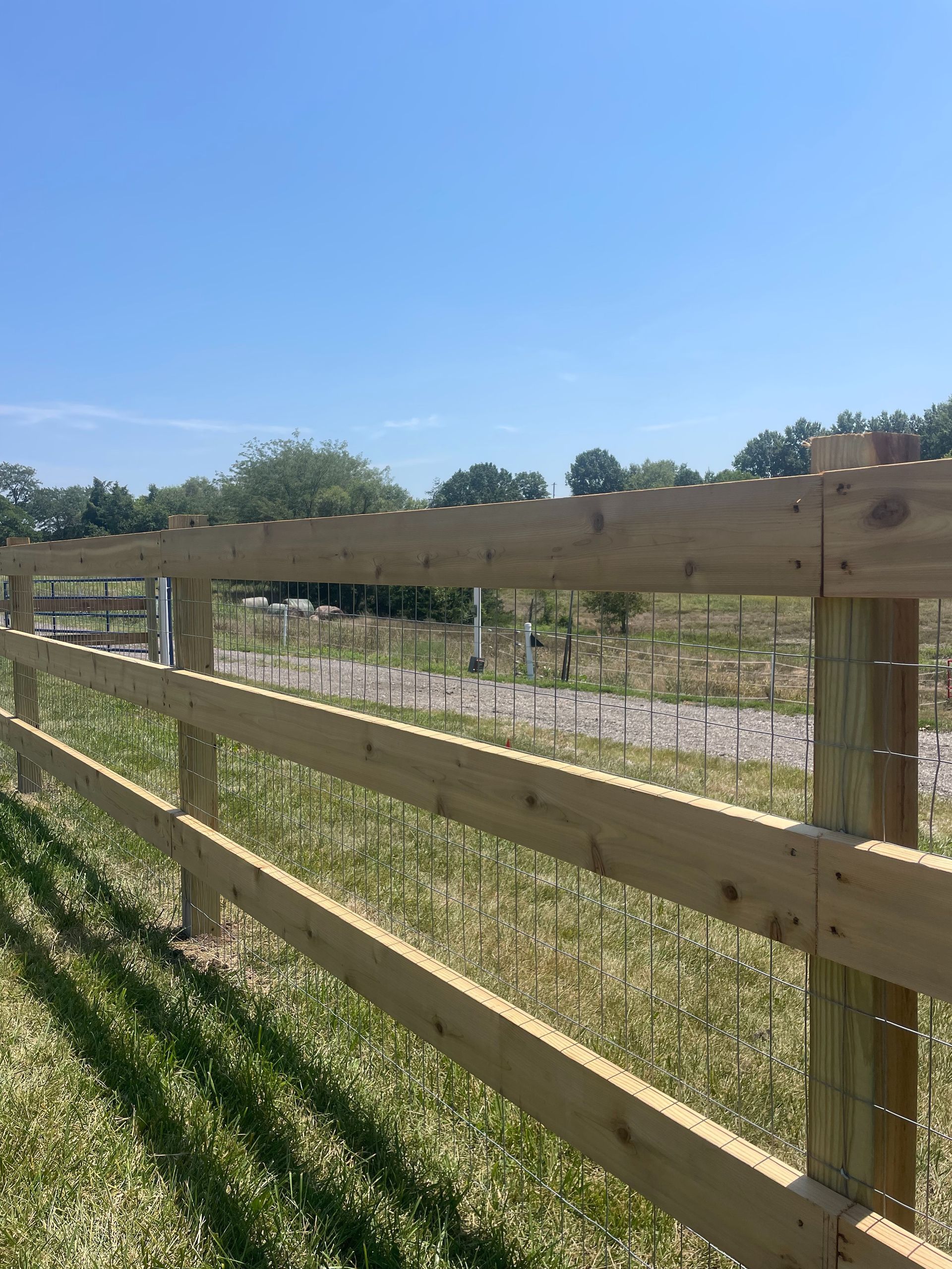 Wooden fence beside a grassy field under a clear blue sky.