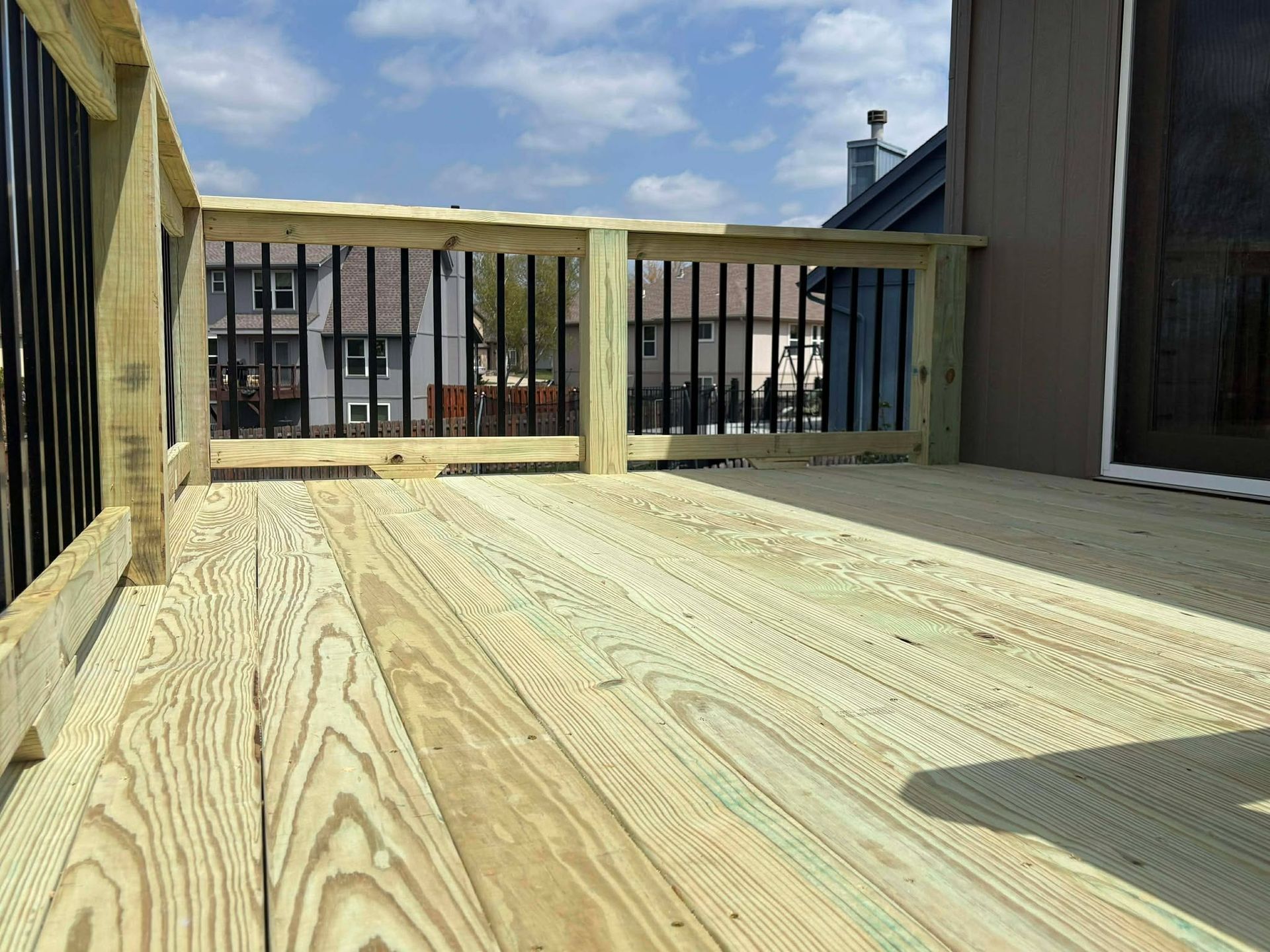 Empty wooden deck with railing, facing neighboring houses under a blue sky.
