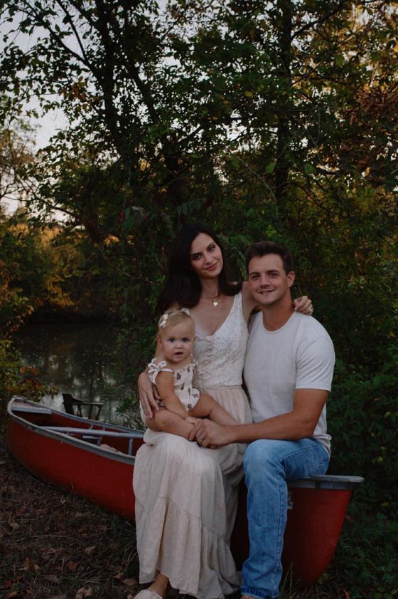 Family sitting in a red canoe by a wooded lakeshore, with a calm outdoor backdrop.
