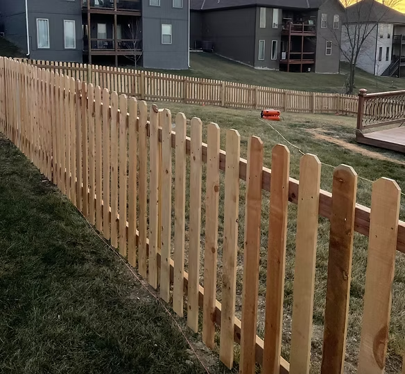 Wooden fence along a grassy slope in a residential neighborhood, with houses in the background.