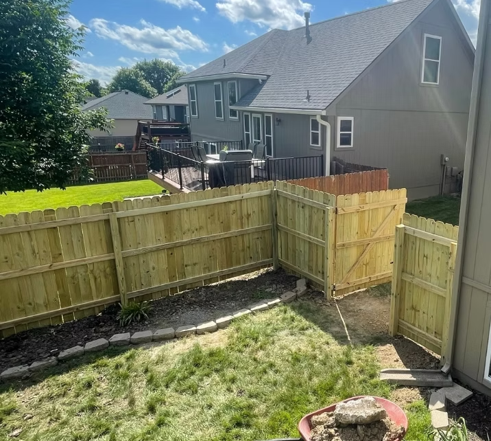 Backyard with new wooden fence, grassy yard, and gray house under a sunny sky