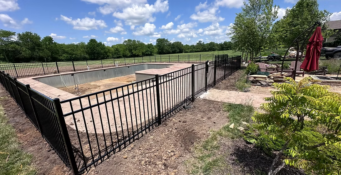 Black metal fence around a raised garden bed under a bright blue sky with trees and patio umbrellas