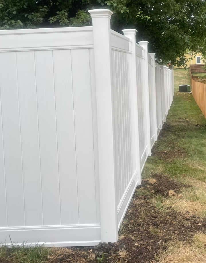 White vinyl privacy fence along a grassy yard beside a wooden fence and trees