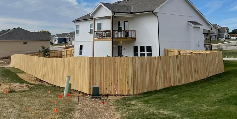 New white house with a wooden privacy fence around a grassy backyard under construction