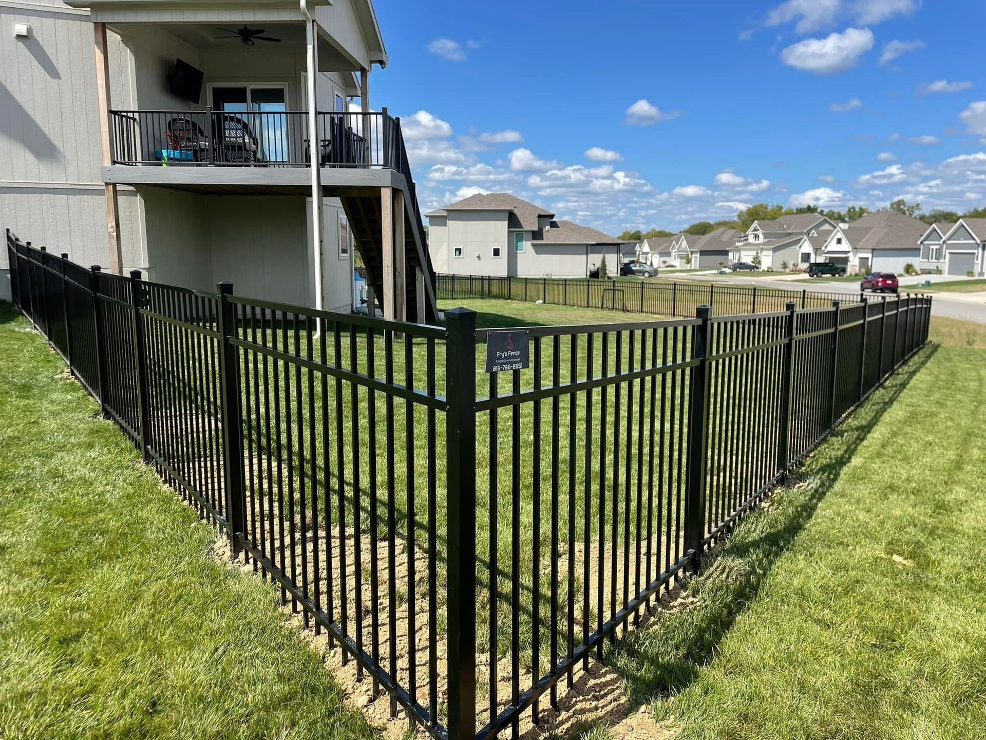 Black metal fence around a grassy backyard beside a two-story house in a suburban neighborhood.