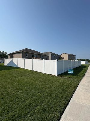 White fenced backyard beside a beige house and sidewalk under a clear blue sky