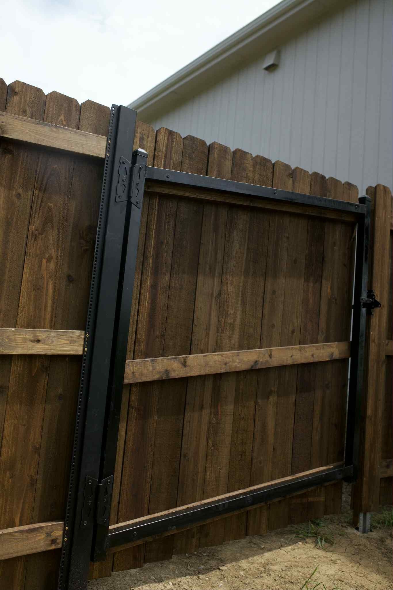 Open black metal gate in a wooden backyard fence beside a house