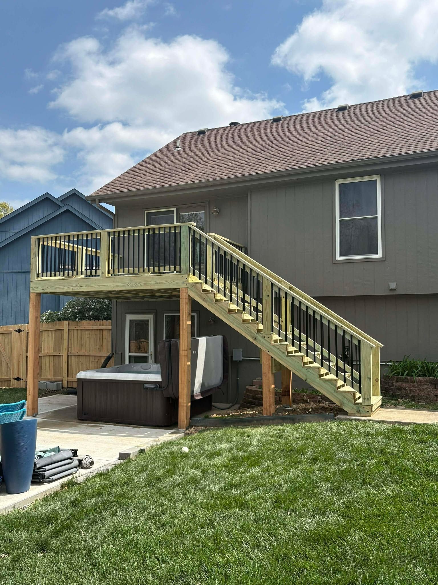 Backyard deck with stairs leading to a gray house, yellow railing, and hot tub below