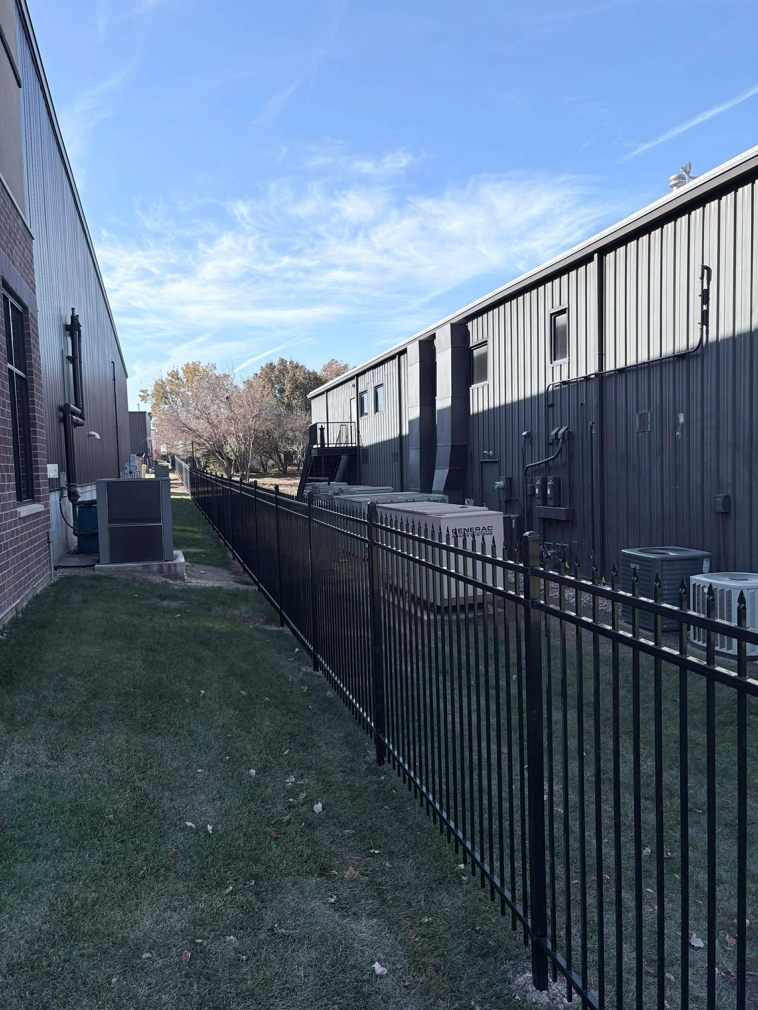 Narrow outdoor corridor beside black fence and building, with artificial grass and blue sky overhead