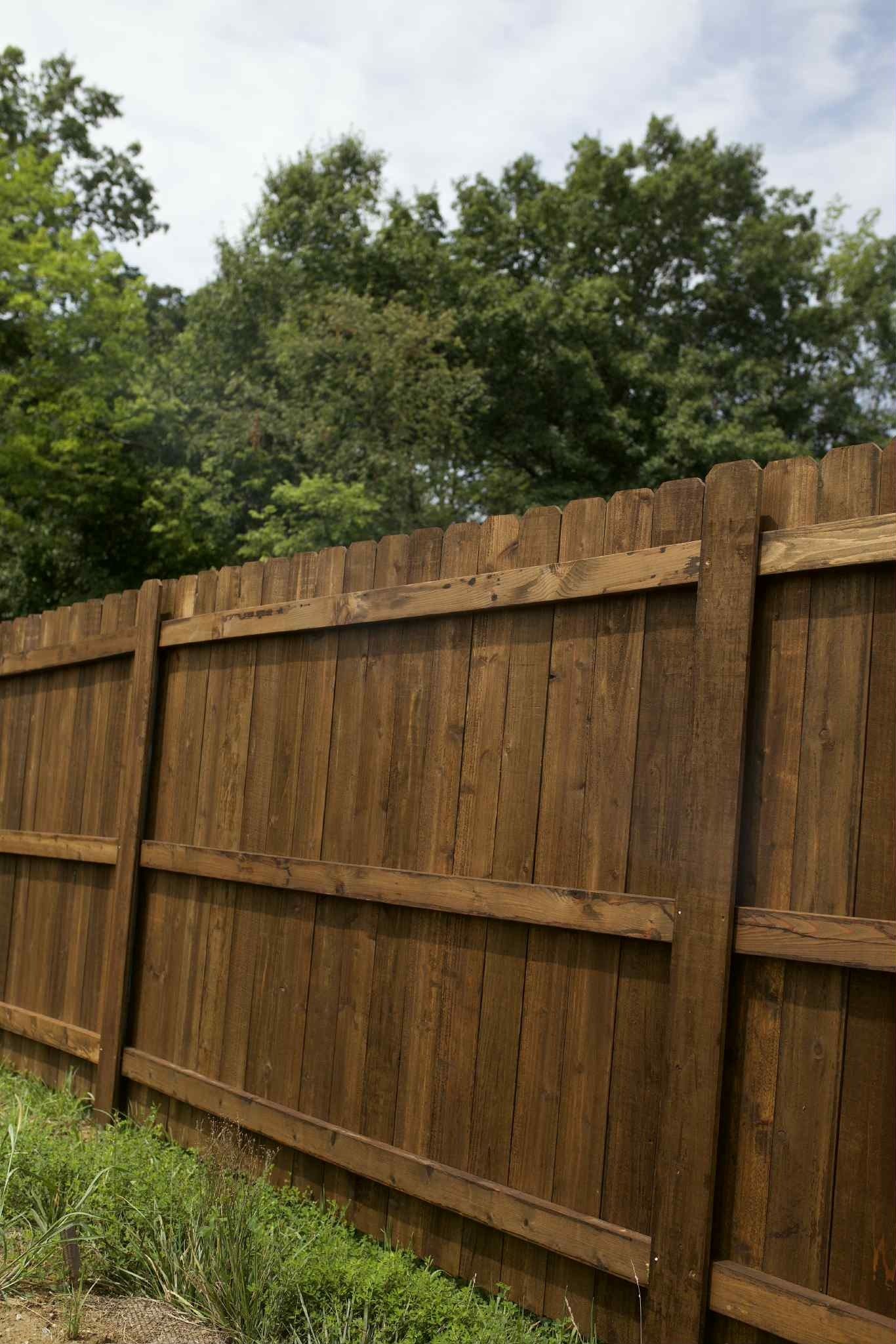 Wooden privacy fence with green trees and cloudy sky in the background