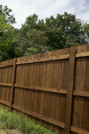 Wooden privacy fence in a yard with trees and cloudy sky behind it