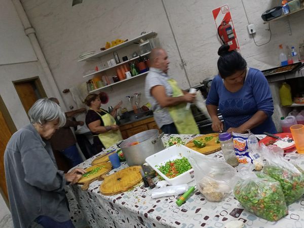 Personas preparando comida en una mesa cubierta de ingredientes en una cocina.