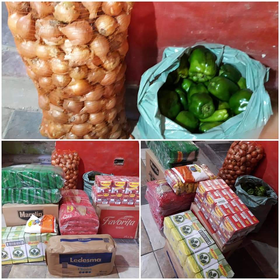 Cebollas y pimientos verdes en bolsas junto a cajas apiladas de productos envasados en un suelo rojo.