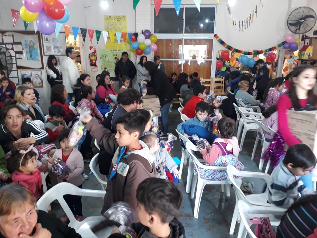Fiesta multitudinaria en un espacio interior decorado, con globos, guirnaldas e invitados sentados.