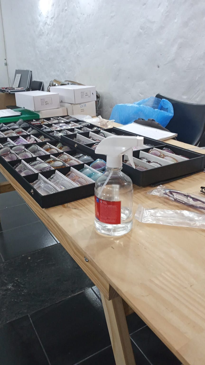 Mesa con bandejas organizadas que contienen objetos pequeños, una botella con atomizador y una bolsa de plástico azul en un taller o trastero.