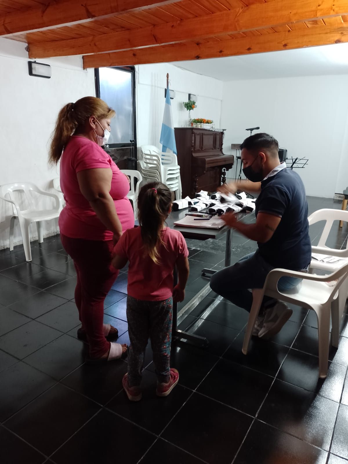 Tres personas alrededor de una mesa en una habitación con poca luz, con un niño de pie junto a ellas.
