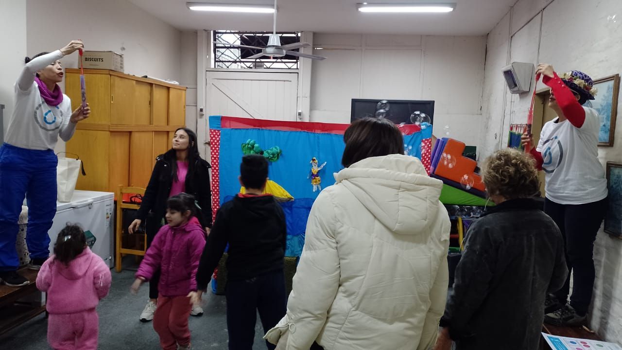 Niños y adultos en un colorido círculo de baile en el aula con los brazos en alto durante una actividad.