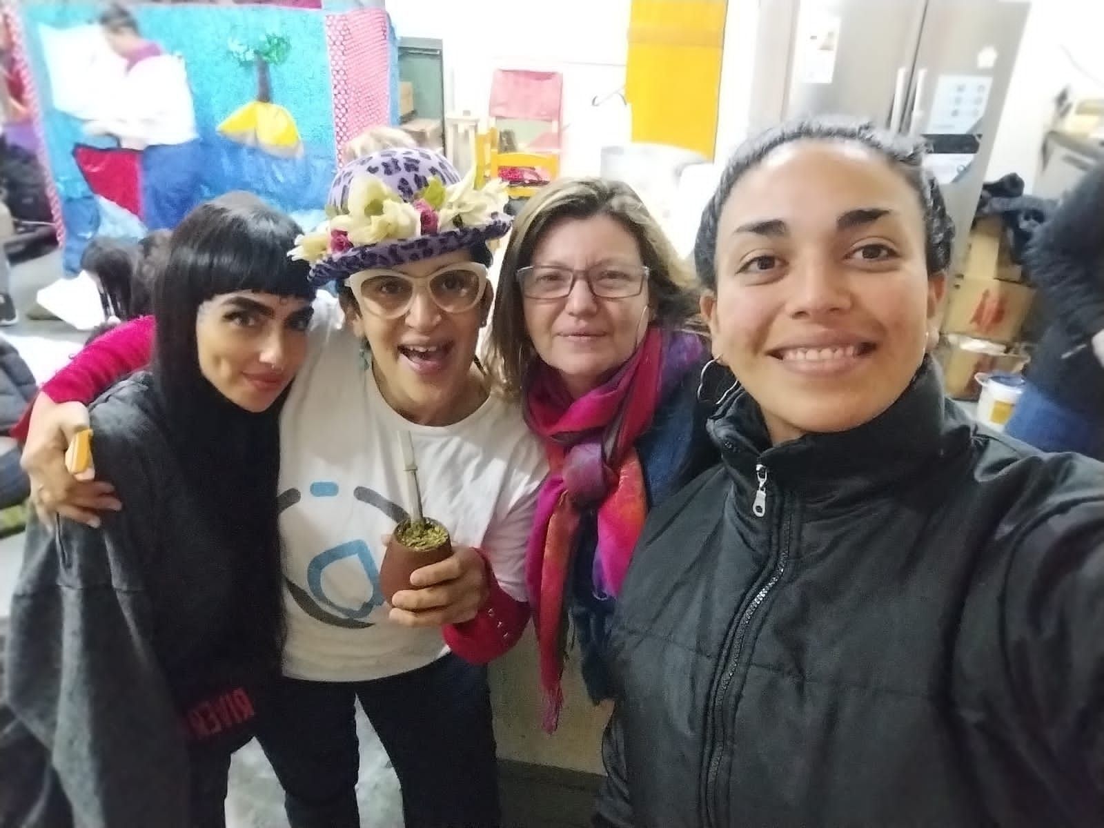 Cuatro personas sonrientes posando en el interior, con un colorido tapiz acolchado de fondo.