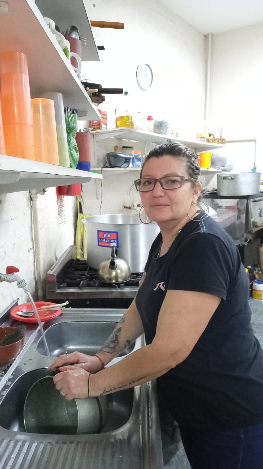 Una persona lavando los platos en el fregadero de una cocina pequeña y desordenada.
