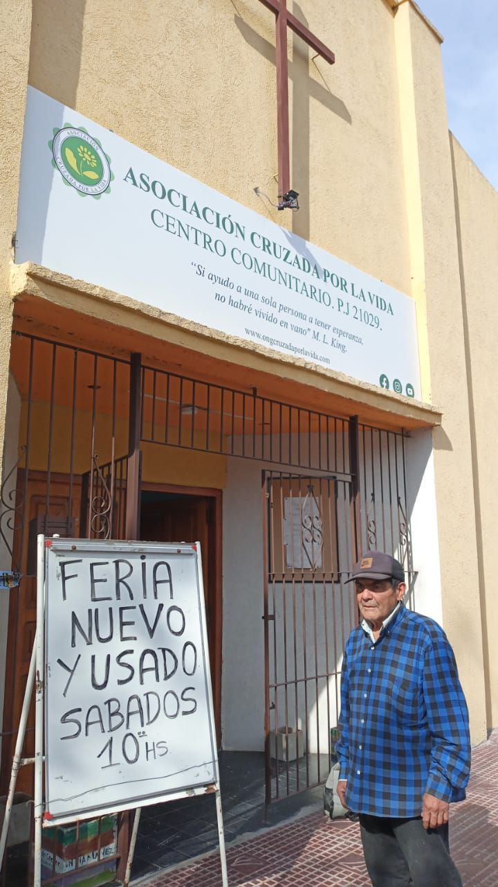 Un hombre está de pie frente a un edificio junto a un cartel que anuncia una feria de muebles usados ​​los sábados a las 10 de la mañana.