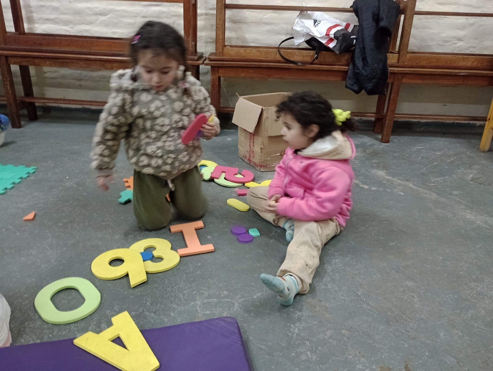 Dos niños jugando con letras de espuma de colores en el suelo de un aula.