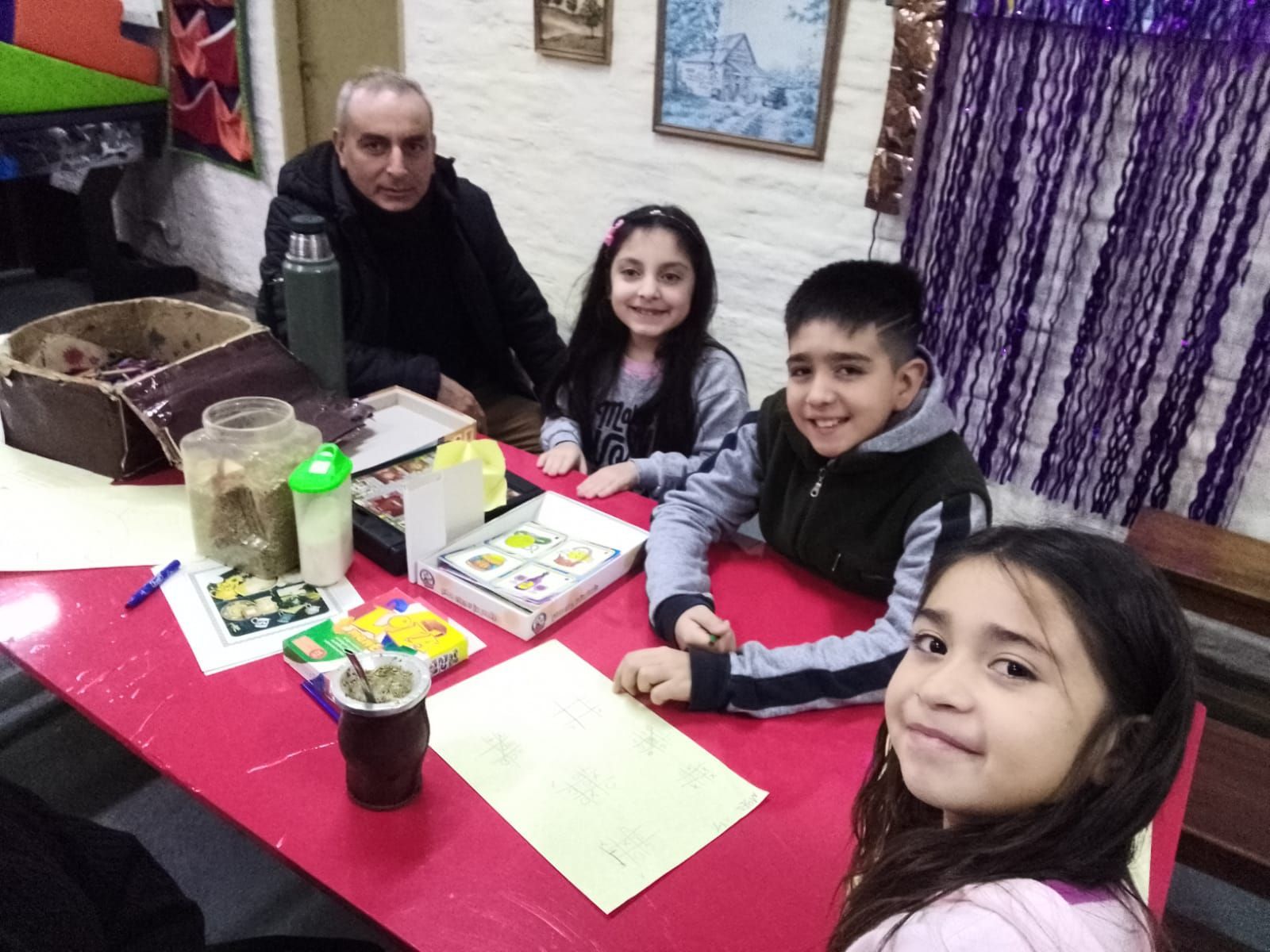 Cuatro personas sentadas en una mesa roja en un acogedor restaurante, sonriendo a la cámara.