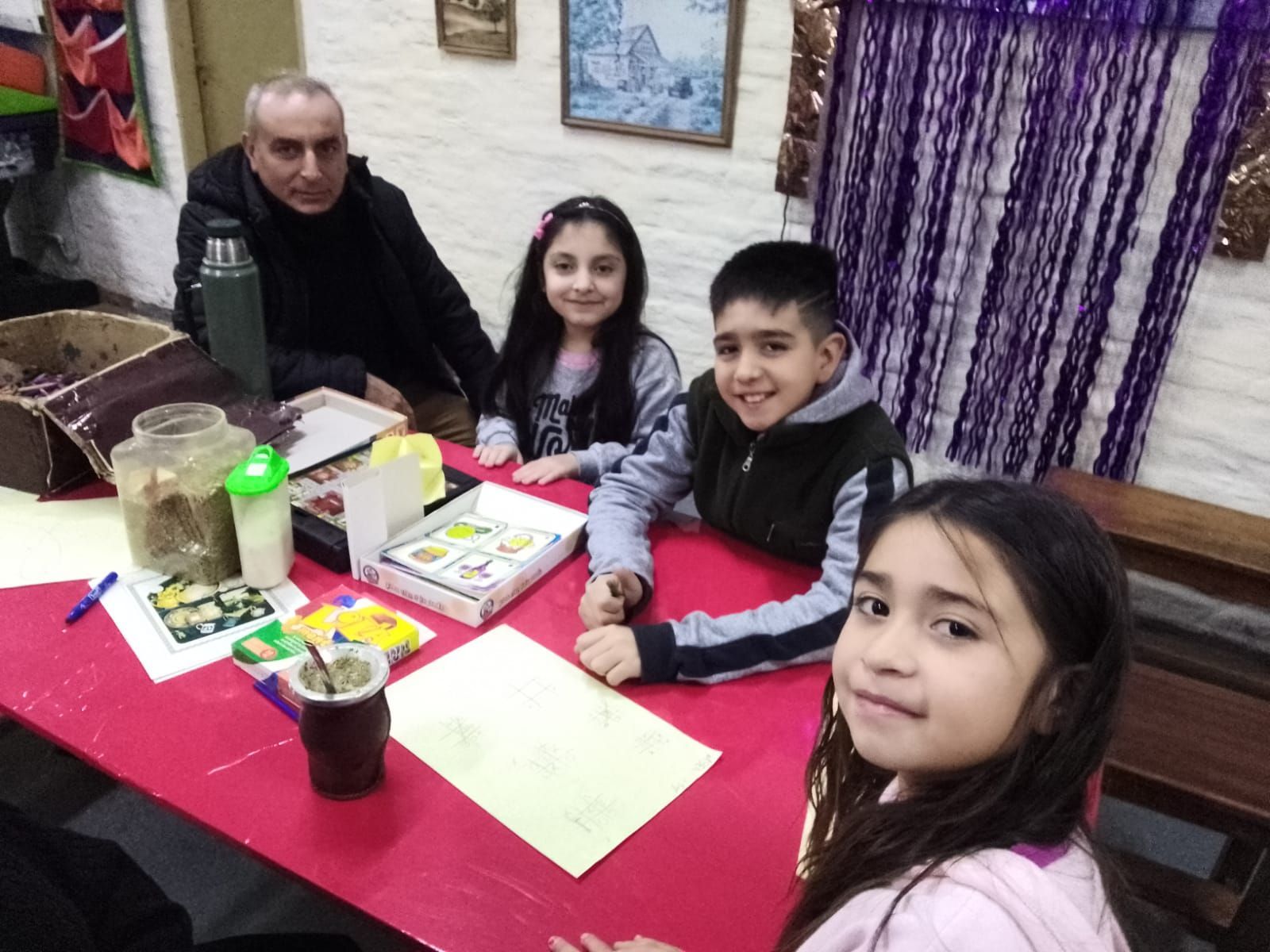Cuatro personas sentadas a una mesa con libros y papeles en una habitación acogedora, sonriendo a la cámara.