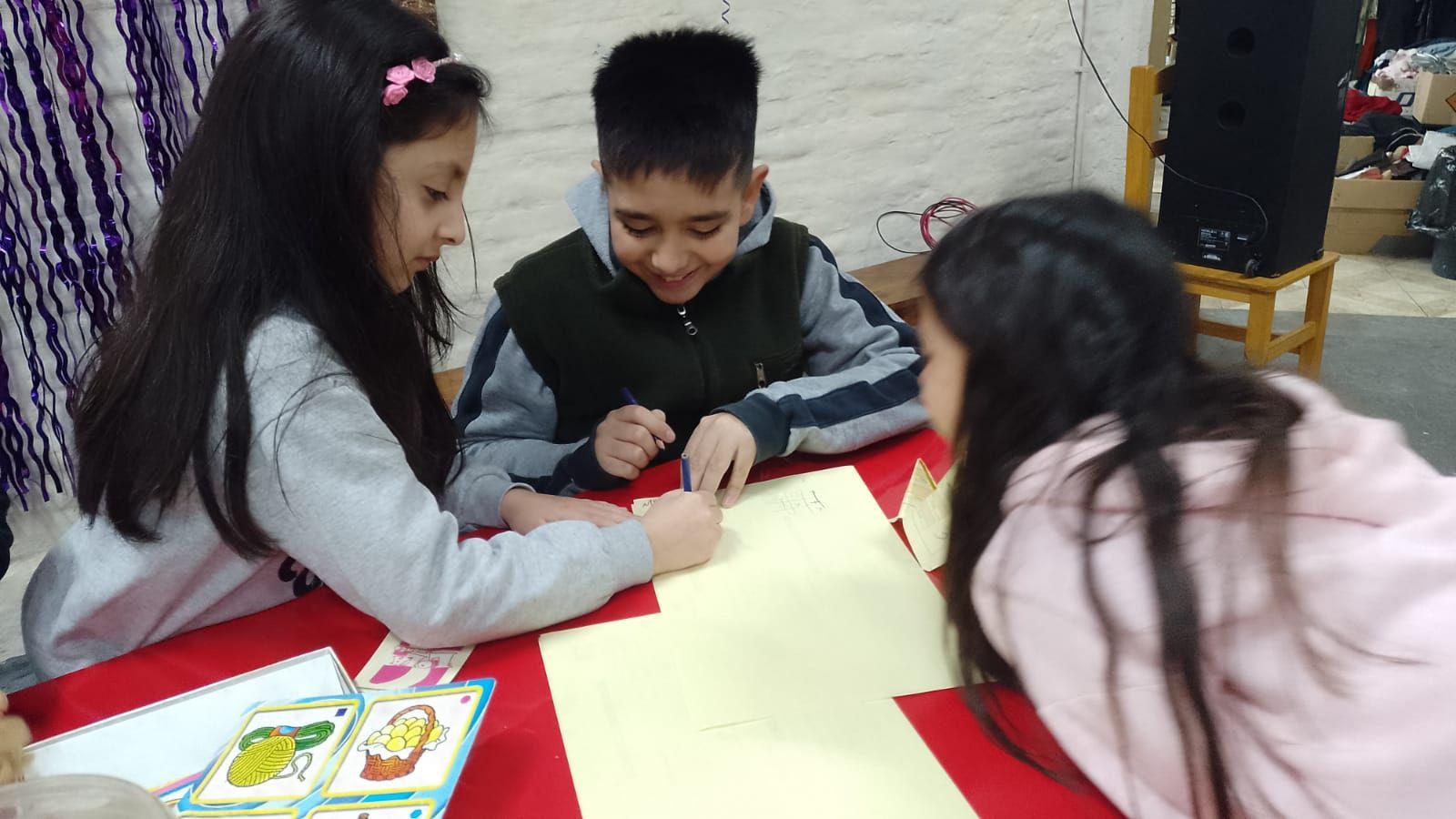 Tres niños se inclinan sobre una mesa y dibujan juntos con rotuladores en un aula.