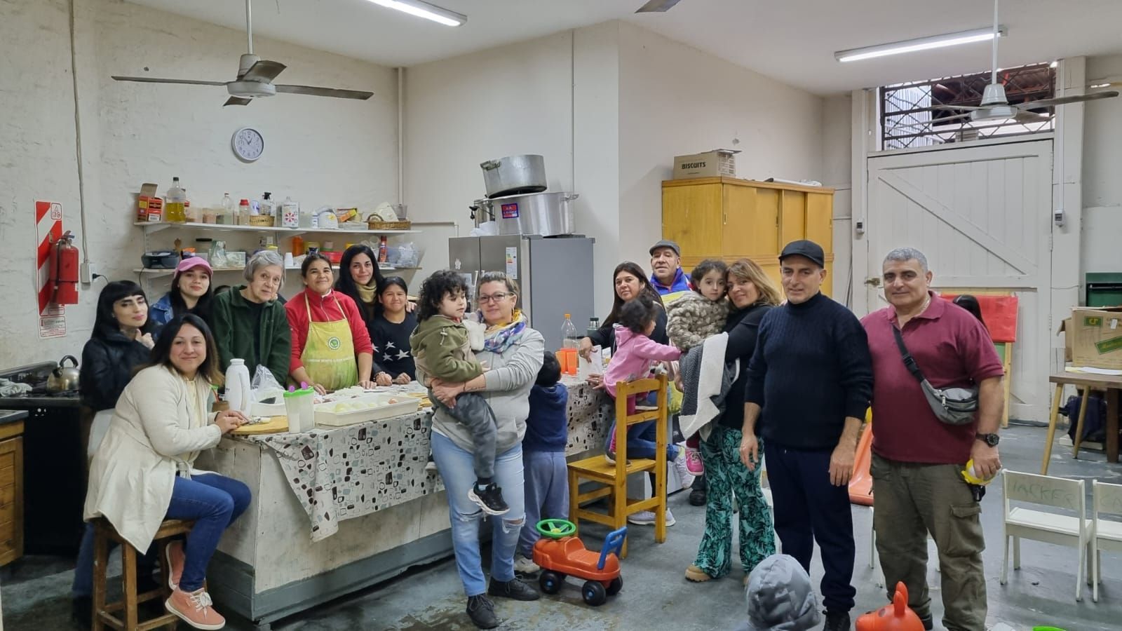 Un grupo de personas se reunió alrededor de la encimera de una cocina en una habitación interior luminosa, posando y sonriendo.